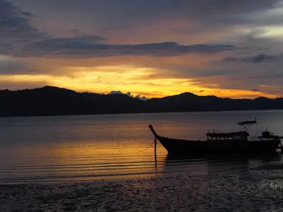 a boat sitting on the beach at sunset at Modern Sunset Sea House Lam Sai in Ko Yao Noi