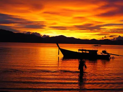 a person walking in the water in front of a boat at Modern Sunset Sea House Lam Sai in Ko Yao Noi
