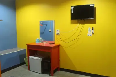a room with a yellow wall with a tv and a desk at Rc Guest House in Phi Phi Don