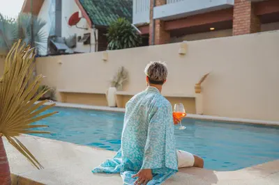 a man sitting next to a swimming pool with a glass of wine at Casa Solana Patong in Patong Beach