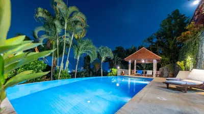 a swimming pool at night with a gazebo and palm trees at Baiyok Villa seaview and edge pool in Patong Beach