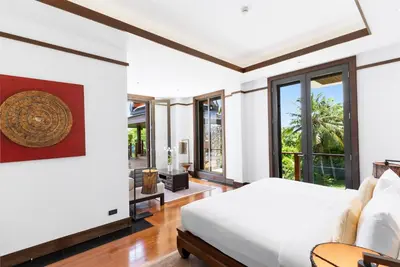 a bedroom with a bed and a living room with windows at Villa Aye in Kamala Beach