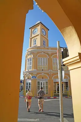 two people walking in front of a building with a clock tower at xx GO INN Phuket Old Town ภูเก็ตโอลทาวน์ ย่านเมืองเก่า in Phuket Town