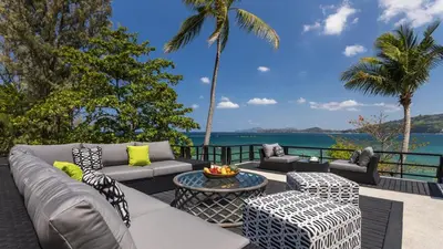 a patio with a couch and chairs and the ocean at Villa Purissara in Phuket Town