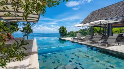 a pool with chairs and the ocean in the background at Villa Saengootsa in Phuket Town
