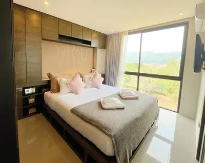 a bedroom with a bed with pink pillows and a window at Citygate in Kamala beach - Perfect Stay for Digital Work in Kamala Beach