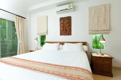 a bedroom with a bed with white sheets and windows at Romanee Villa by G Estate in Rawai Beach
