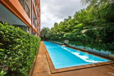 a swimming pool in front of a building with trees at New Condo NaiHarn Beach by Capital Pro in Phuket Town