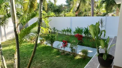a garden with palm trees and a white fence at Jasmine Village in Rawai Beach
