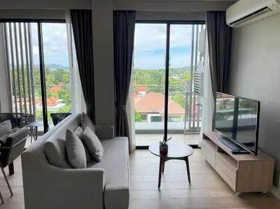 a living room with a couch and a large window at Mountain view apartment in the heart of BangTao in Bang Tao Beach