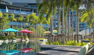 a hotel with a pool with palm trees and umbrellas at 2 bdr Apartment in Mida Grande Surin Beach by CapitalPro in Phuket Town