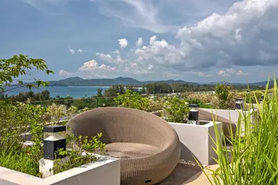 a rattan chair sits on a patio overlooking the water at 3 bdr SeaView Apartment walking to Surin Beach by CapitalPro in Phuket Town