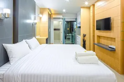 a bedroom with a large white bed and a tv at Chalong - Studio Service Apartment - Phoomjai in Ban Klang