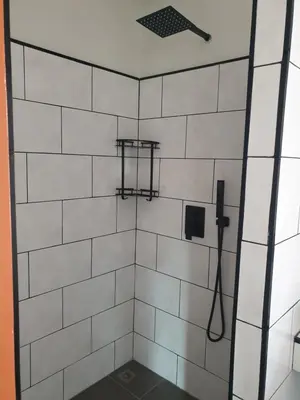 a white tiled shower with a black and white tile wall at My Friend's House Villa in Karon Beach