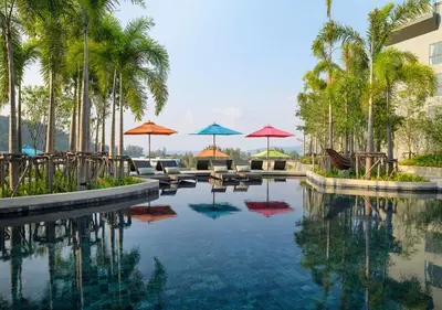 a swimming pool with umbrellas and chairs and palm trees at Уютные апартаменты в Mide Grant in Phuket Town