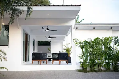 a white house with a patio with chairs and a table at Private Pool Villa Rawai Beach in Rawai Beach