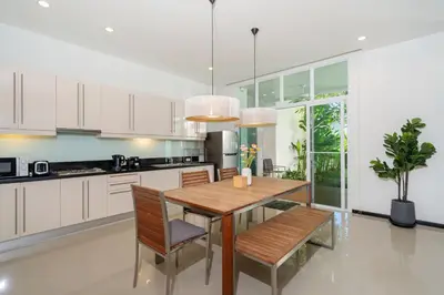 a kitchen with white cabinets and a wooden table and chairs at Tropical Garden Villa - Oxygen Bangtao Beach in Bang Tao Beach
