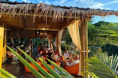 a group of people sitting at a restaurant under a thatch roof at Greenheart Garden View Camp Phuket in Kata Beach