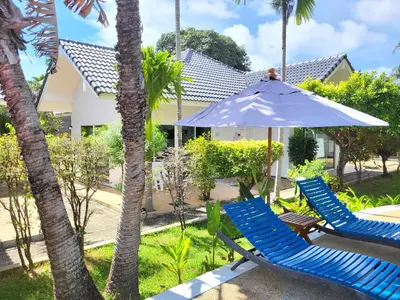 a couple of blue chairs and an umbrella and palm trees at Blue Palm Kata Resort in Kata Beach