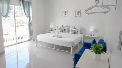 a white bedroom with a bed and a blue chair at Cinderella Residence in Patong Beach