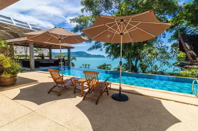 a table and chairs with umbrellas next to a swimming pool at Aoyon Beach, a 5-bedroom Thai-style villa with stunning sea views, 50 meters direct beach access, free maid, in Phuket Town
