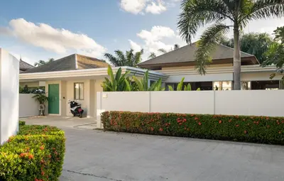a house with a white fence and a palm tree at 3-Bedroom Pool Villa in Trichada Bangtao in Bang Tao Beach