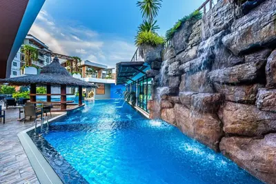 a pool in a resort with a rock wall at Chalong Miracle Lakeview in Chalong