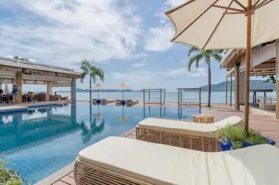a swimming pool with an umbrella next to a resort at Poppy Beachfront Residence in Rawai Beach