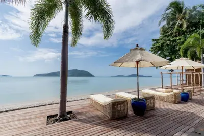 a wooden deck with chairs and an umbrella and the ocean at Olive 1 Bedroom Beachfront in Rawai Beach