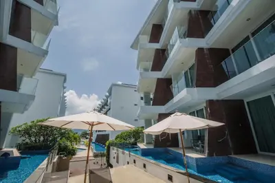 two umbrellas and a swimming pool in front of a building at Maroon Studio at the beachfront in Rawai Beach