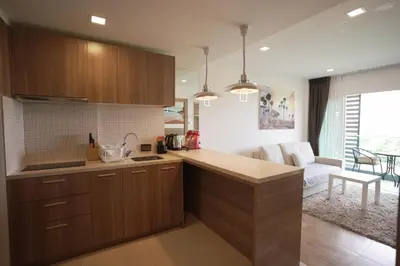 a kitchen with wooden cabinets and a living room at Calypso Condo Rawai Nai Harn beach in Rawai Beach