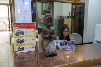 a woman sitting at a table with a statue on a counter at Little Mermaid Guesthouse & Restaurant in Kata Beach
