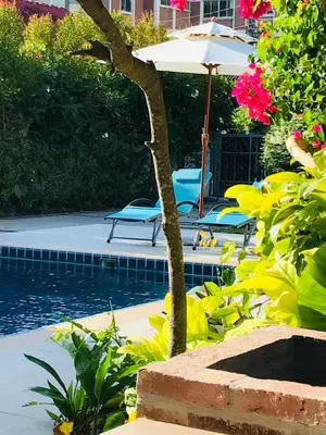 a swimming pool with an umbrella and chairs and flowers at Guest House, shared pool, private bathroom and kitchen in Phuket Town