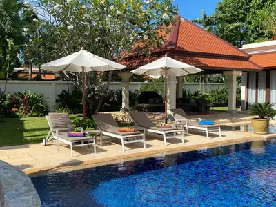 a swimming pool with lounge chairs and umbrellas next to a swimming pool at Luxury Sai Taan Villa in Bang Tao in Bang Tao Beach
