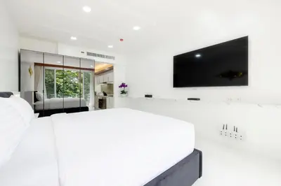 a white bedroom with a large bed and a flat screen tv at Rudi Condo by Q Conzept in Kata Beach