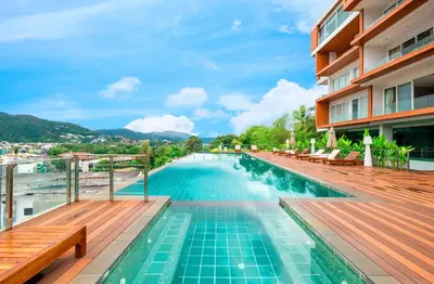 a pool at a hotel with wooden decking and benches at Rudi Condo by Q Conzept in Kata Beach