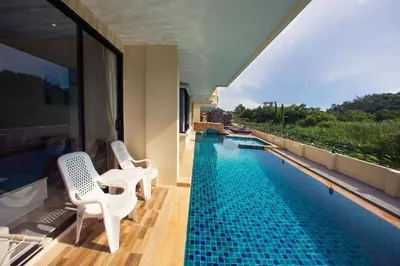 a swimming pool with two white chairs next to a building at 2 bed room the lago naiharn beach in Nai Harn Beach