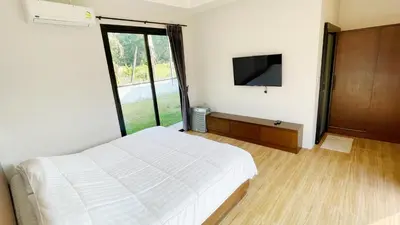 a bedroom with a white bed and a television at Spacious Private Villa Modern Style near beach in Thai Muang