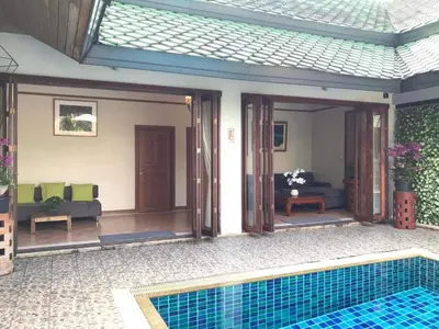 a house with a swimming pool and a living room at Plumeria Villa Thalang in Ban Pak Lak