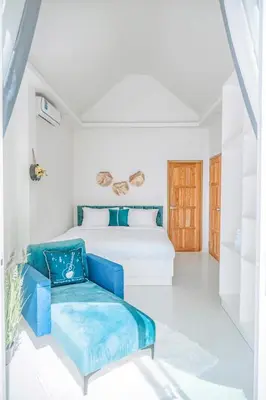 a white bedroom with a bed and a blue chair at Mr Oh's Seaview House Phuket AoYon in Phuket Town