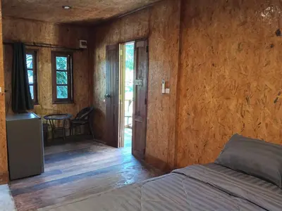 a bedroom with a bed and a table and windows at Sukanyawoodhouse in Ban Tha Rua