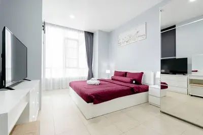 a white bedroom with a red bed and a television at Apartment Karon 62 sq in Karon Beach