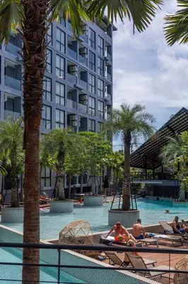 a hotel swimming pool with palm trees and people on lounge chairs at Modern Condo in Boutique Style Resort CGB4 in Phuket Town