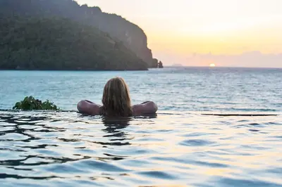 a woman floating in the water at sunset at The Cobble Beach Hotel- Phi Phi Island in Phi Phi Don