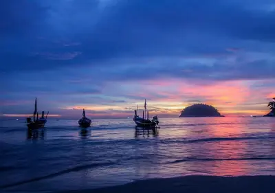 three boats sitting in the water at sunset at The Blue Bay Experience in Kata Beach