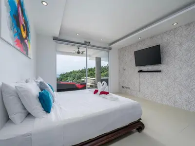 a bedroom with a large white bed with a tv on the wall at The Blue Bay Experience in Kata Beach