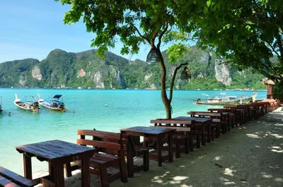a row of benches on a beach with boats in the water at Phi Phi Rimlay Resort in Phi Phi Don