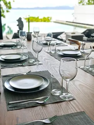 a wooden table with plates and wine glasses on it at Luxury Beachfront AMANA Villa 4 Br at Ta-Ke Residence A in Phuket Town
