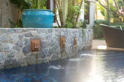a swimming pool with a stone retaining wall and a water fountain at Saitaan Villa Dennapa Bang Tao Beach in Bang Tao Beach