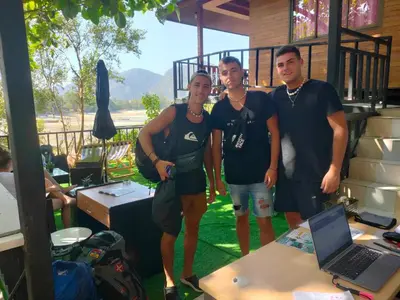 a group of three men standing next to a table with a laptop at Sweed Dee Seaview Hostel in Phi Phi Don